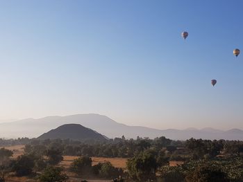 Hot air balloons flying in mountains against clear sky