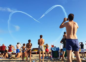 Rear view of people standing against blue sky