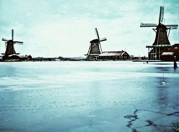 Traditional windmill on snow covered landscape against sky