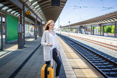 Young woman with luggage waiting at railroad station platform