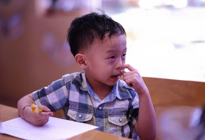 Cute boy picking nose while sitting with book at table