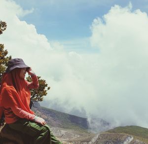 Side view of woman looking away while sitting against mountain and sky