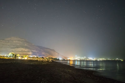 Illuminated city by sea against sky at night