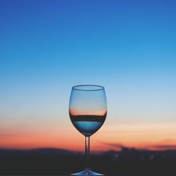 Close-up of wineglass against blue sky during sunset