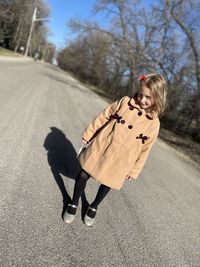 Low section of a girl wearing a brown coat walking on road in fall