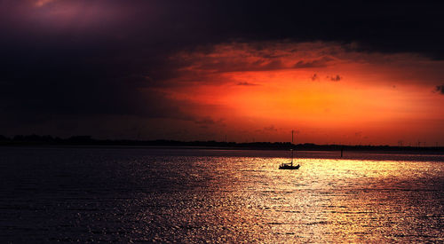 Silhouette boat sailing in sea against dramatic sky during sunset