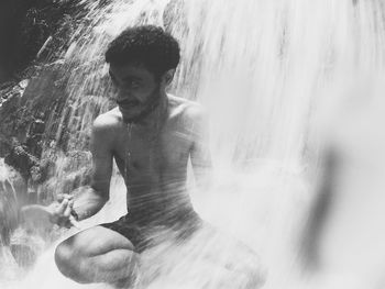 Young man splashing water in waterfall