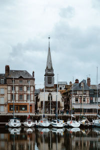 Sailboats moored on river by buildings against sky in city