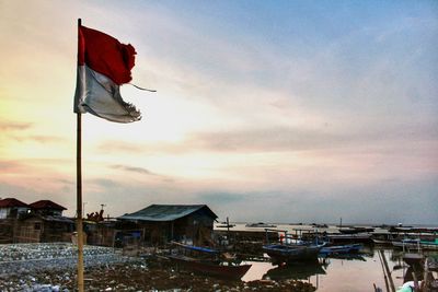 Flag by buildings against sky during sunset