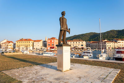 Male statue at harbor in city against clear blue sky