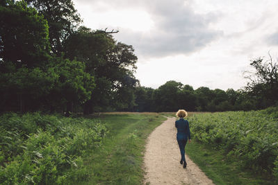 Rear view of woman walking on pathway amidst field against sky