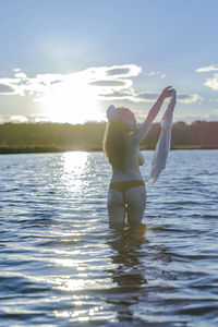 Woman with arms raised in sea against sky