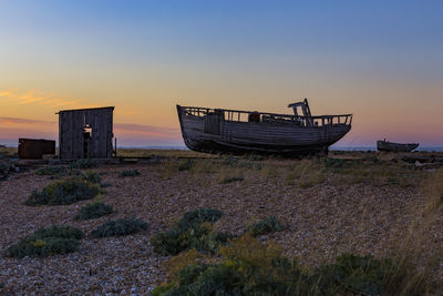 Abandoned boat moored on shore against sky during sunset