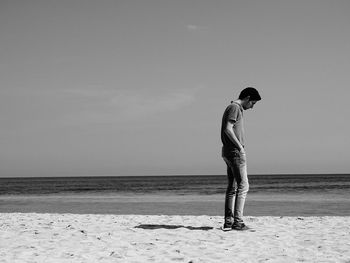 Full length of man looking down while standing at beach against sky