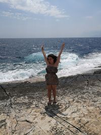 Woman with arms raised standing at beach against sky