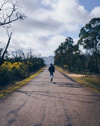 Rear view of man walking on road against sky