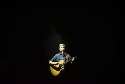 Man playing guitar against black background