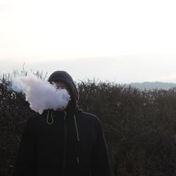 Man exhaling smoke at field against sky