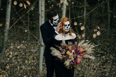 A couple in love celebrates halloween in costumes and makeup with a bouquet of dried flowers