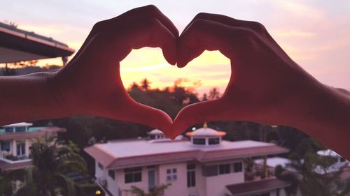 Cropped hands of woman making heart shape during sunset