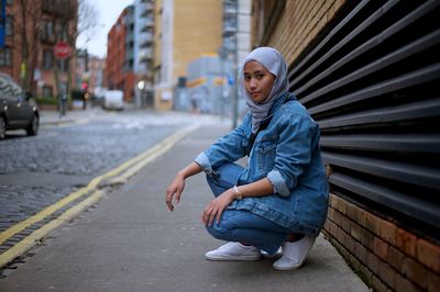 Portrait of woman in hijab crouching on footpath