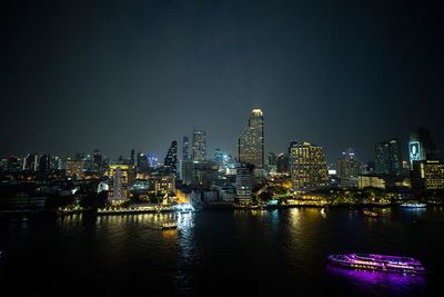 Illuminated buildings by river against sky at night