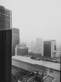 Buildings in city against sky seen through glass window