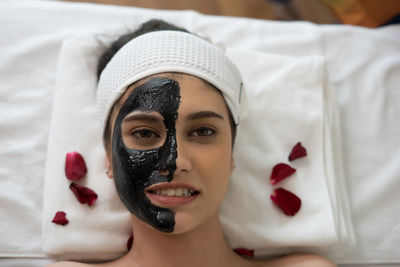 Directly above portrait of young woman with facial mask lying on massage table