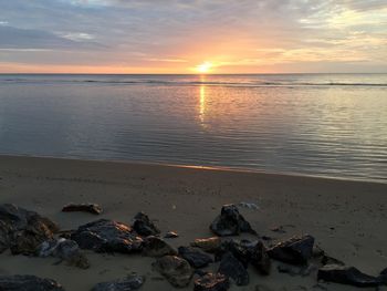 Wet stones on shore at beach against sky during sunset