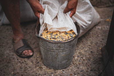 An elderly man pours wheat from a bag into a bucket.