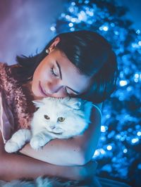 Woman embracing cat against illuminated christmas tree at home