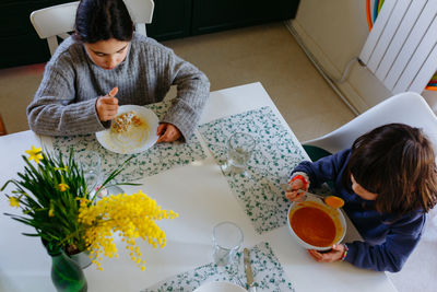 Upper view of two sisters eating lunch at home at white table with yellow flowers