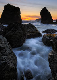 Rocks on sea shore against sky during sunset