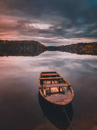 Boat moored in lake against sky during sunset