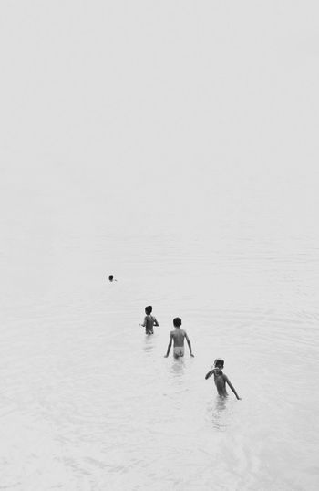 PEOPLE SWIMMING IN SEA AGAINST SKY