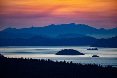 Scenic view of sea and silhouette mountains against orange sky