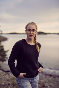 Portrait of young woman standing at beach against sky