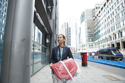 Smiling businesswoman holding shopping clothes while walking on street in city