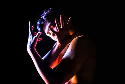 Close-up of hands against illuminated light over black background