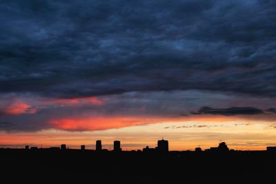 Silhouette buildings against dramatic sky during sunset