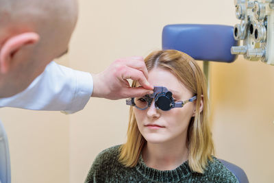 A male optometrist checks the eyesight of a young girl with a trial frame