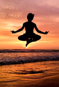 Silhouette man jumping on beach against orange sky