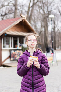 Cute girl with glasses eats a pie bought in a food truck in a city park. takeaway food