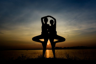Silhouette friends doing yoga at beach against sky during sunset