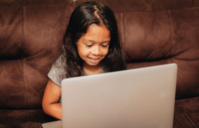 Cute girl using laptop while sitting on sofa at home