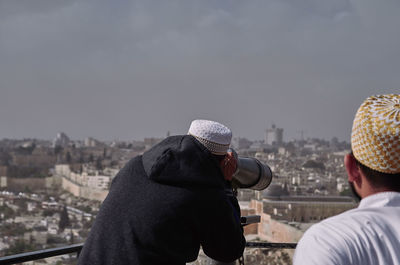 Rear view of man looking at city buildings against sky