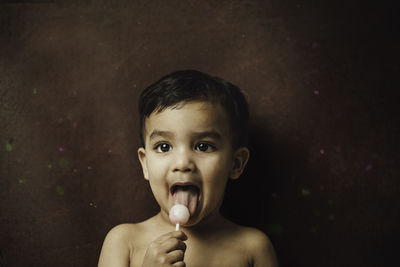 Close-up of boy eating lollipop while standing against wall