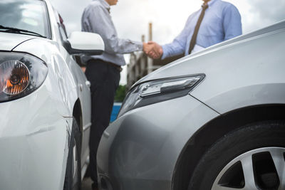 Midsection of customer shaking hands with car dealer outdoors