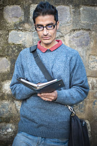 Man reading book while standing against stone wall