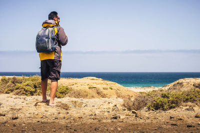 Rear view of man standing on shore against sky